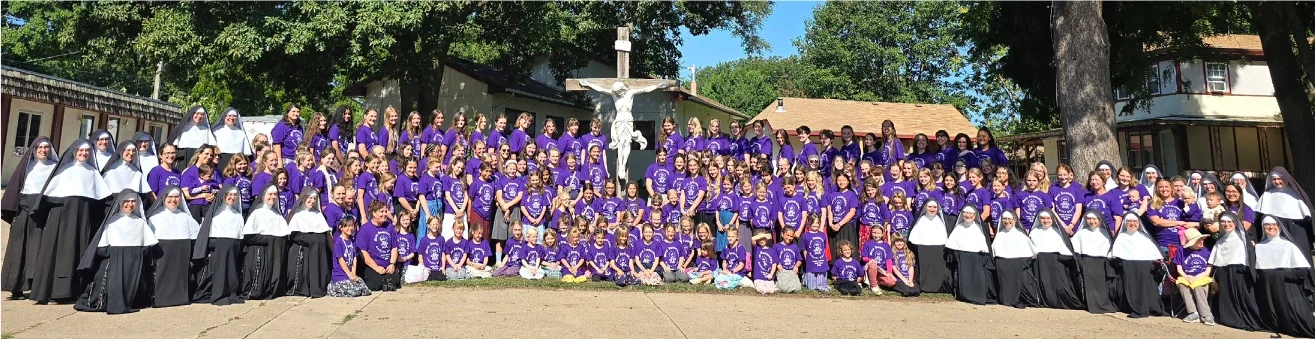 Sisters and a large group gathered outdoors around a crucifix.